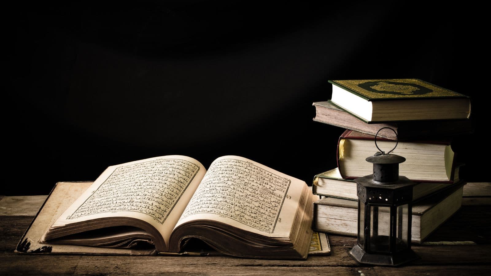 Coran ouvert, livres anciens et lanterne sur une table en bois